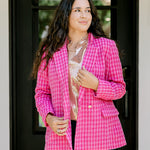Woman with dark hair wearing a pink tweed blazer with gold buttons. Model paired blazer with dark-wash denim jeans. 