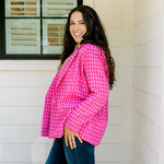 Woman with dark hair wearing a pink tweed blazer with gold buttons. Model paired blazer with dark-wash denim jeans. 