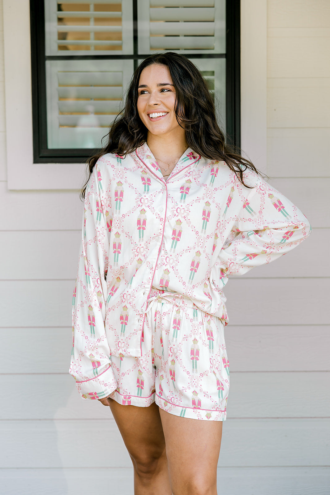 Woman with dark hair wearing a long-sleeve top and shorts pajama set featuring nutcracker graphics. 