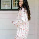 Woman with dark hair wearing a long-sleeve top and shorts pajama set featuring nutcracker graphics. 