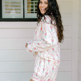 Woman with dark hair wearing a long-sleeve top and shorts pajama set featuring nutcracker graphics. 