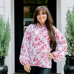 Woman with dark hair wearing a long-sleeve red & cream Santa toile graphics top. Model paired this top with leather pants. 