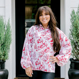 Woman with dark hair wearing a long-sleeve red & cream Santa toile graphics top. Model paired this top with leather pants. 