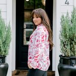 Woman with dark hair wearing a long-sleeve red & cream Santa toile graphics top. Model paired this top with leather pants. 