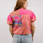 Woman wearing a colorful patterned shirt with a plain background faceing back 