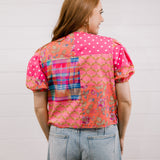 Woman wearing a colorful patterned shirt with a plain background faceing back 