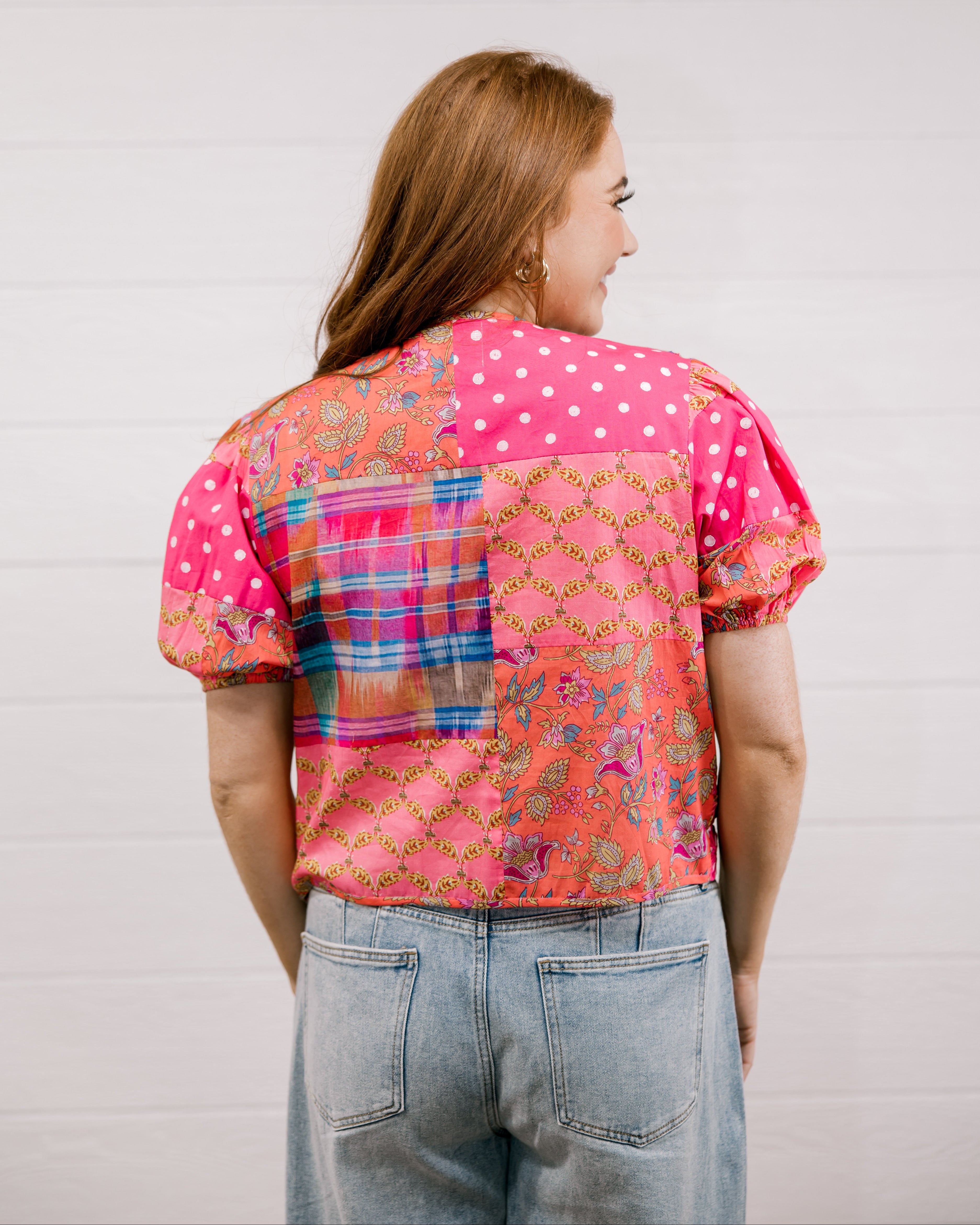 Woman wearing a colorful patterned shirt with a plain background faceing back 