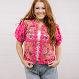 Woman wearing a pink floral patchwork vest against a plain background facing front.