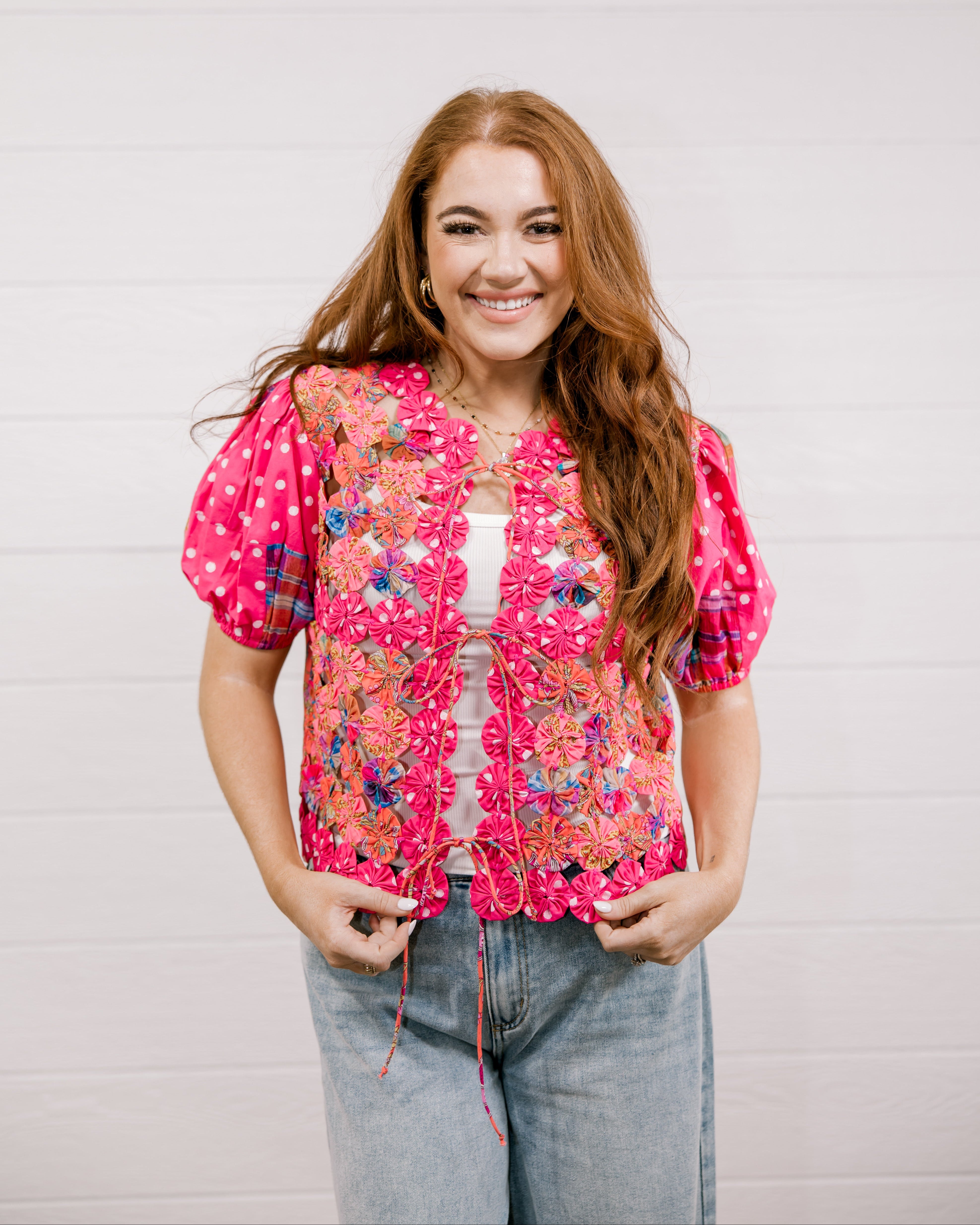 Woman wearing a pink floral patchwork vest against a plain background facing front.