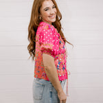Woman wearing a bright pink floral blouse against a light background side