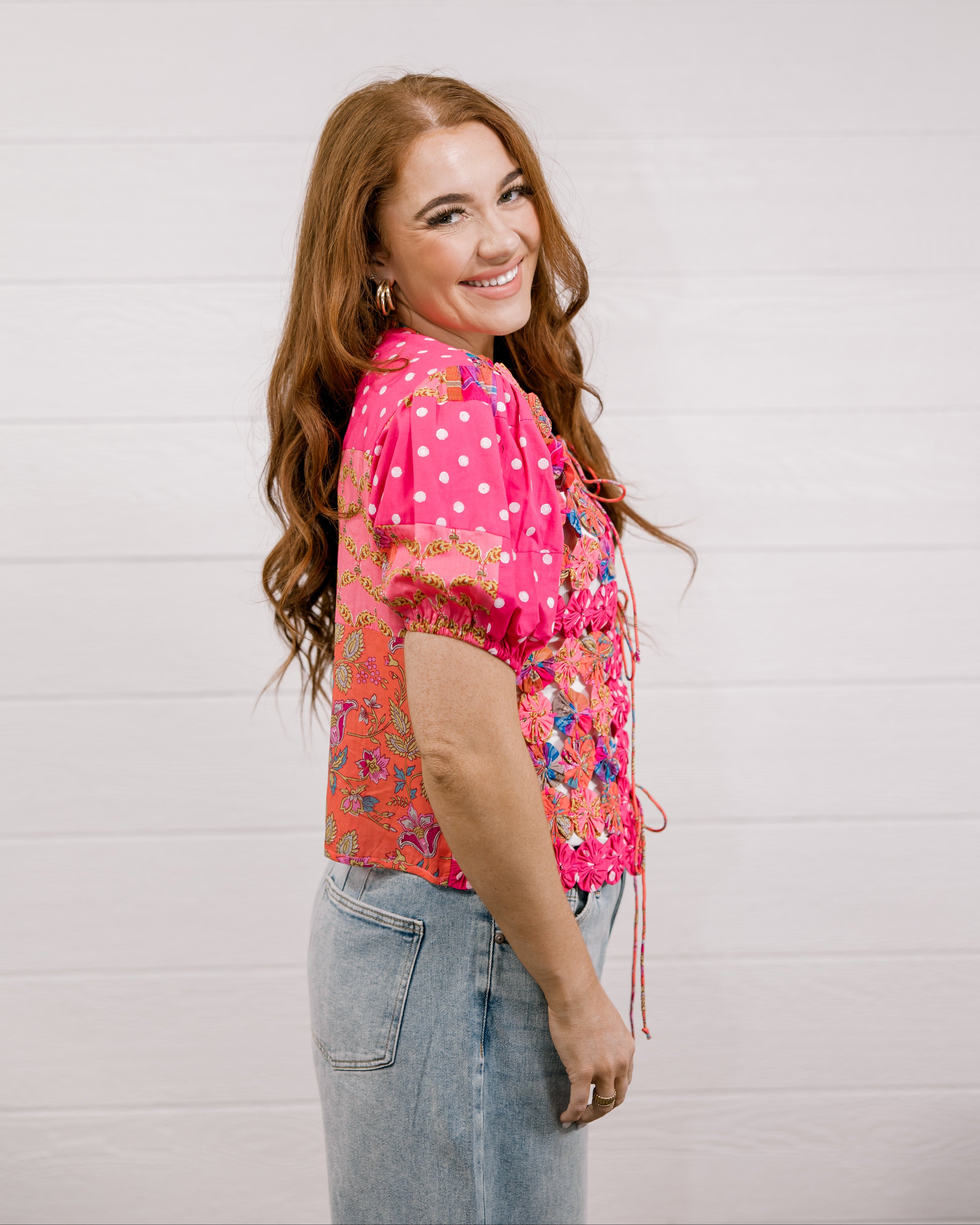Woman wearing a bright pink floral blouse against a light background side