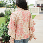 Woman with dark hair wearing a poncho style top with floral patchwork and light-wash denim jeans. 