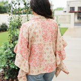 Woman with dark hair wearing a poncho style top with floral patchwork and light-wash denim jeans. 