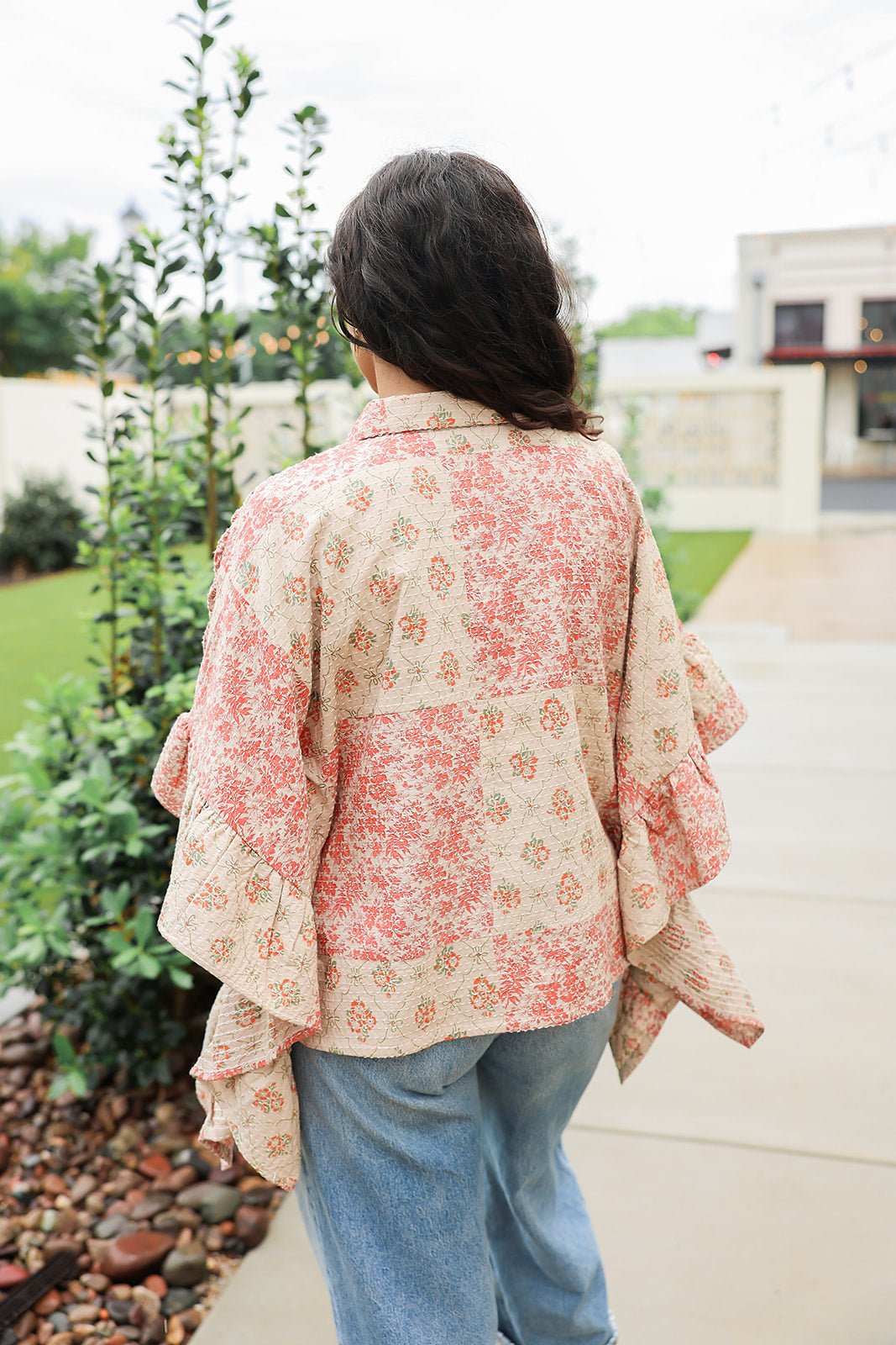 Woman with dark hair wearing a poncho style top with floral patchwork and light-wash denim jeans. 