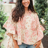 Woman with dark hair wearing a poncho style top with floral patchwork and light-wash denim jeans. 