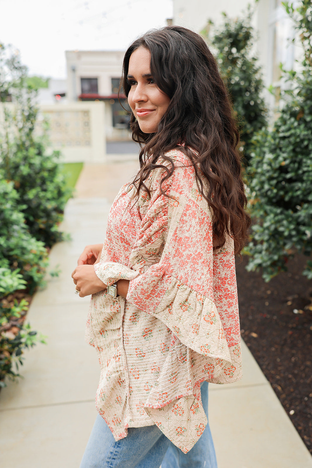 Woman with dark hair wearing a poncho style top with floral patchwork and light-wash denim jeans. 