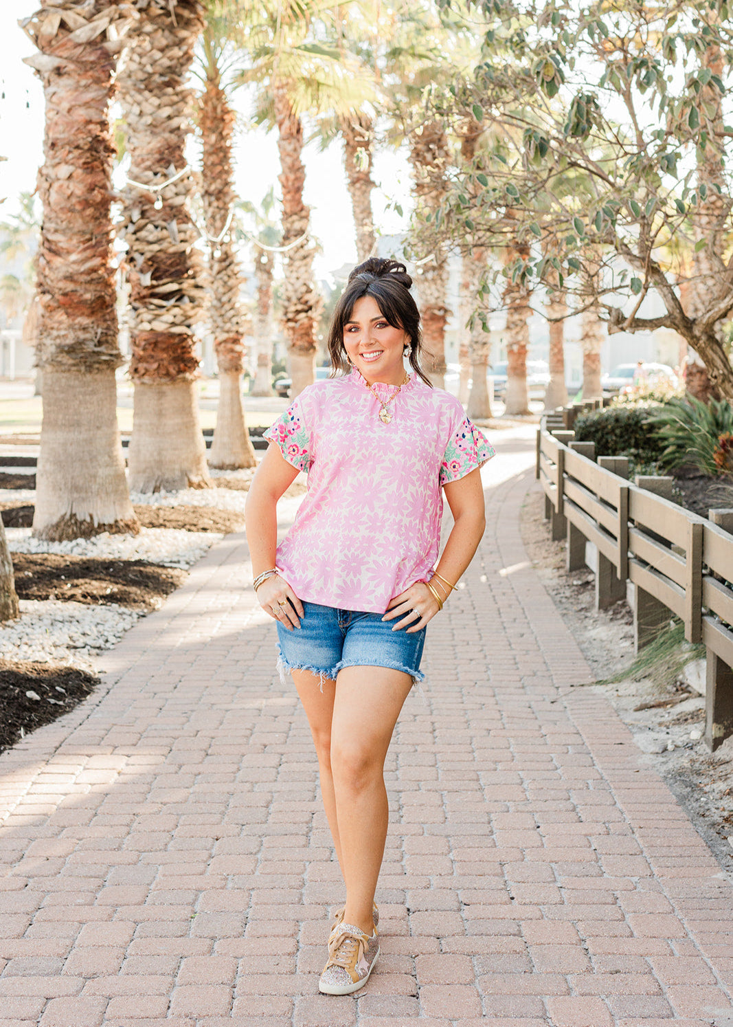 Woman with dark hair standing in a front profile position wearing the Hallie Top in a lifestyle themed background. The focal point of the image is the model wearing the top in "real time" with emphasis on the entire outfit. The model paired this outfit with dark-wash denim shorts. 