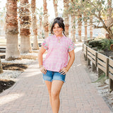 Woman with dark hair standing in a front profile position wearing the Hallie Top in a lifestyle themed background. The focal point of the image is the model wearing the top in "real time" with emphasis on the entire outfit. The model paired this outfit with dark-wash denim shorts. 