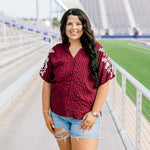 Woman with dark hair standing in a front profile position wearing the Havanah Top at a football field. The focal point of this image is the front details of the top including embroidery down shoulders, high-collar, and v-neckline. The model paired this top with light-wash denim shorts. 