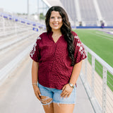 Woman with dark hair standing in a front profile position wearing the Havanah Top at a football field. The focal point of this image is the front details of the top including embroidery down shoulders, high-collar, and v-neckline. The model paired this top with light-wash denim shorts. 