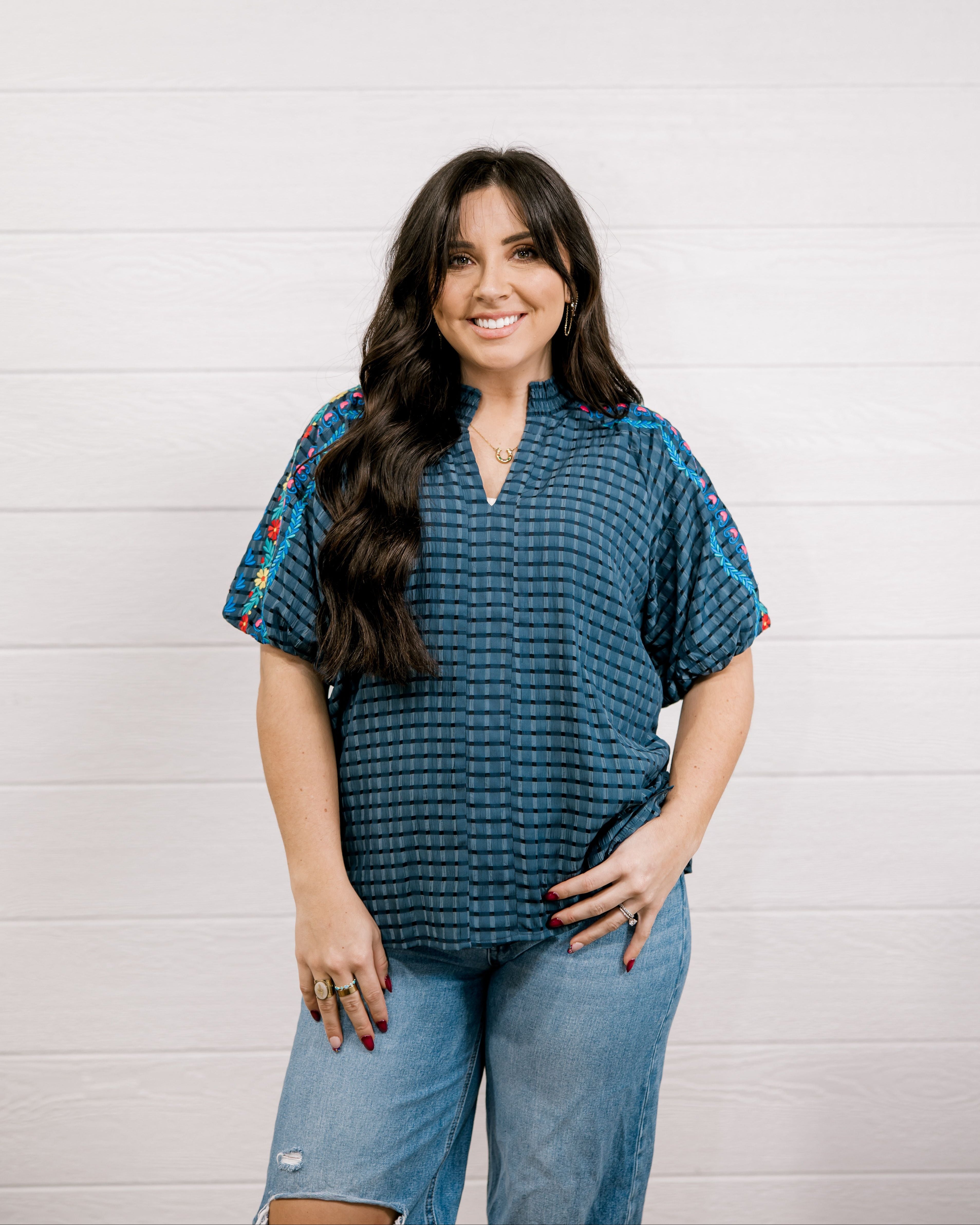 Women wearing a navy shirt with embroidery on the sleeves with a slit V neck against a white background showing the front 