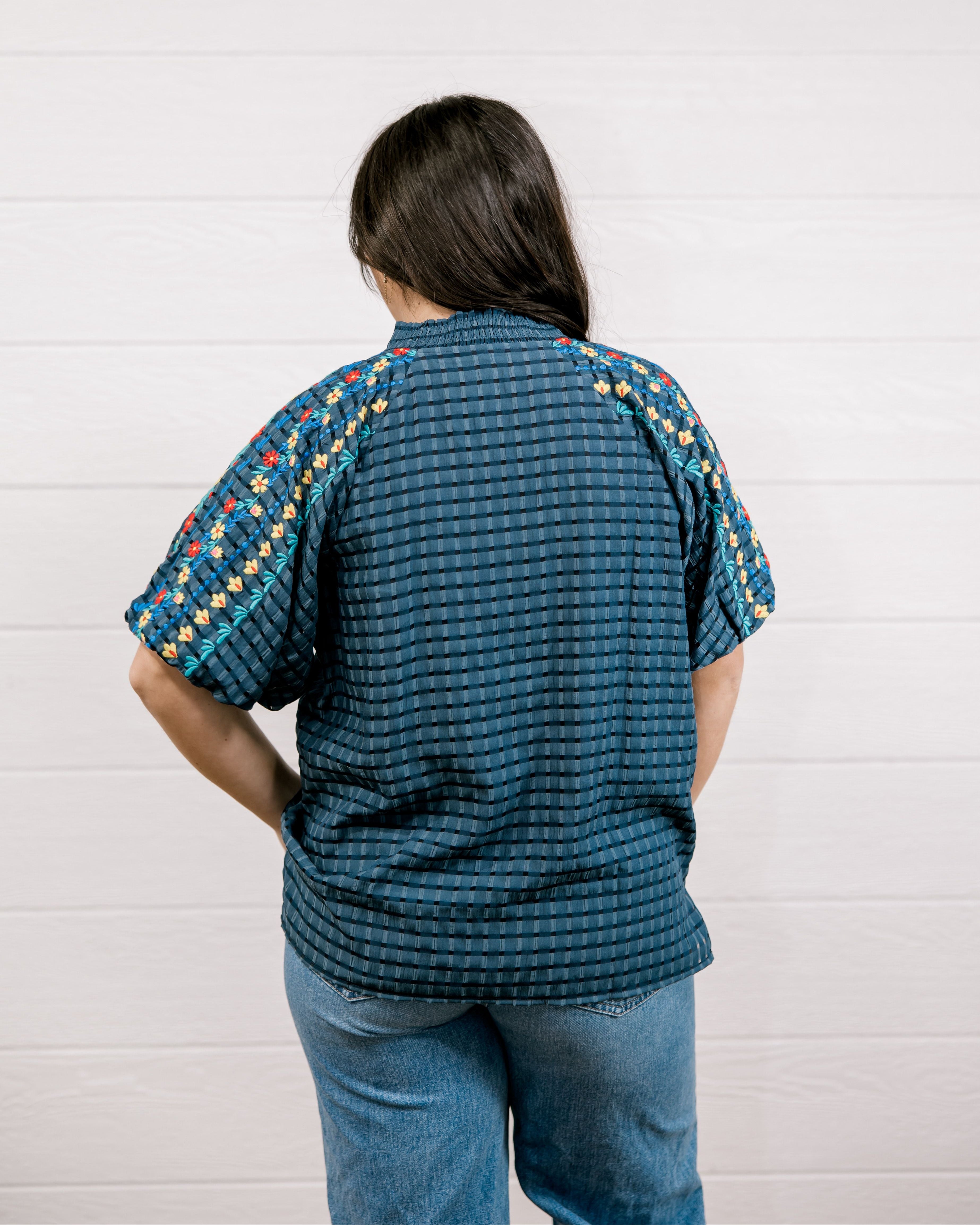A women wearing a navy top showing the back and fit with detailed embroidery on a white background 