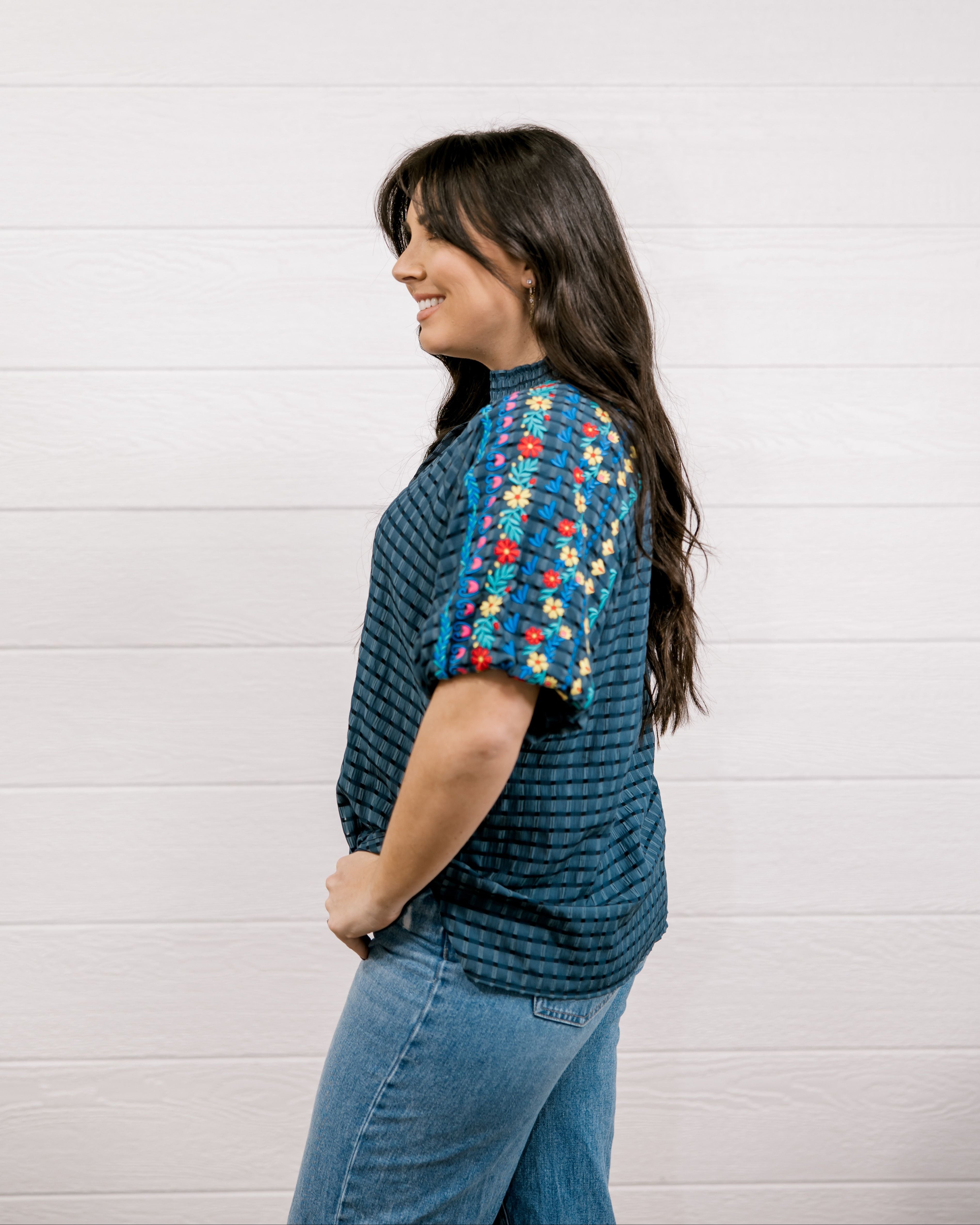 Women wearing a navy shirt showing the side and the detailed embroidery on the sleeve on a white background 
