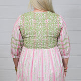 Woman with blonde hair wearing a above-the-knee dress with pink and green floral graphics, and green embroidery on quarter-sleeves, chest, and shoulders. 