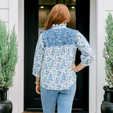 Woman with red hair wearing a quarter-sleeve top with blue Santa toile graphics and blue embroidery on shoulders and chest. Model paired this top with denim jeans.