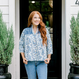 Woman with red hair wearing a quarter-sleeve top with blue Santa toile graphics and blue embroidery on shoulders and chest. Model paired this top with denim jeans.