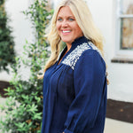 Woman with blonde hair wearing blue quarter sleeve blouse with white embroidery on front and back. and a burnt orange skirt.