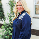 Woman with blonde hair wearing blue quarter sleeve blouse with white embroidery on front and back. and a burnt orange skirt.