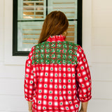 Woman with red hair wearing a quarter-sleeve top with red plaid graphics and green embroidery. Model paired this top with light-wash denim jeans. 