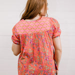 Woman wearing a floral blouse with a plain background facing back. 