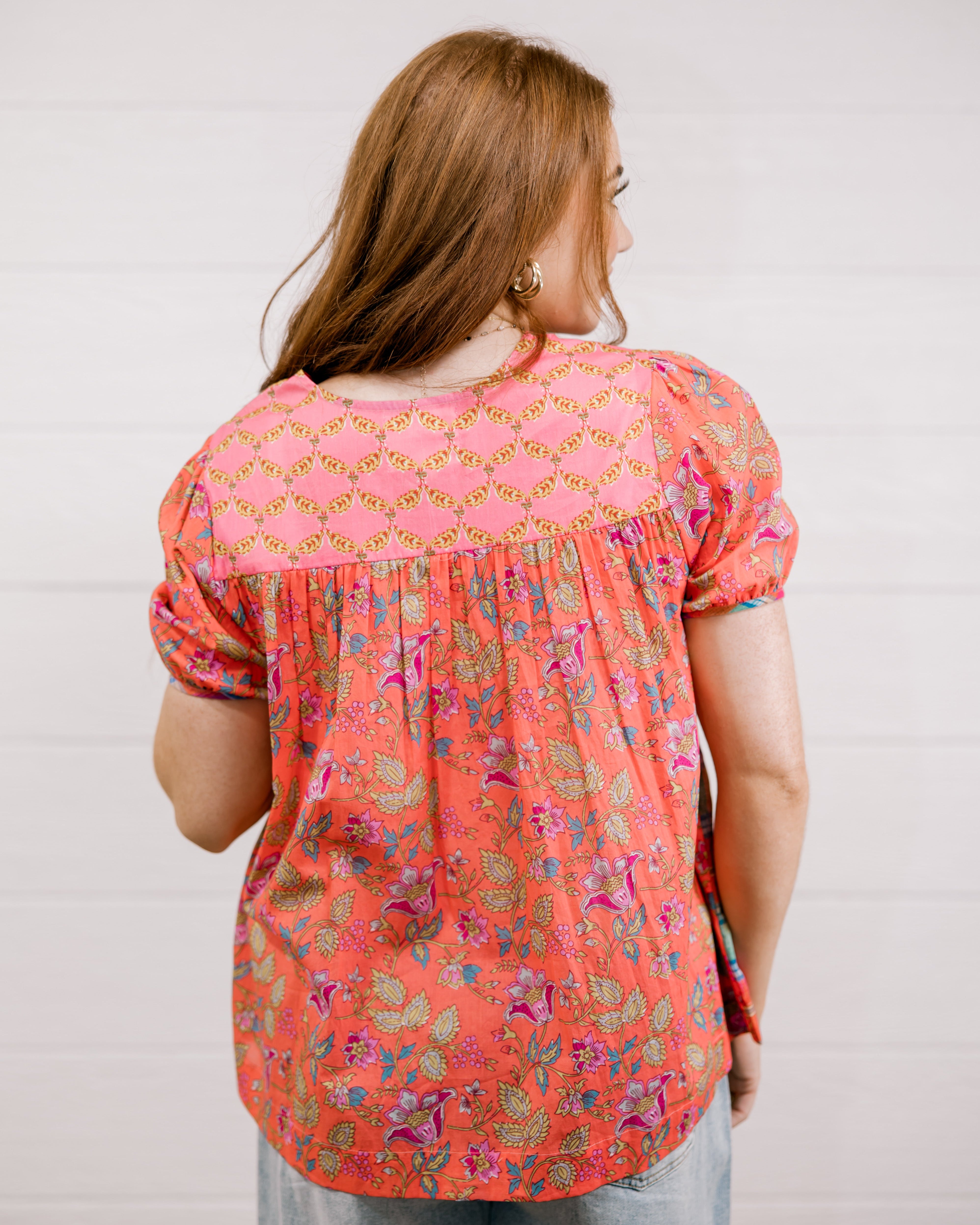 Woman wearing a floral blouse with a plain background facing back. 
