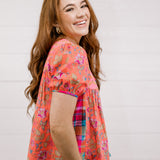 Woman wearing a colorful floral blouse against a plain background facing side. 