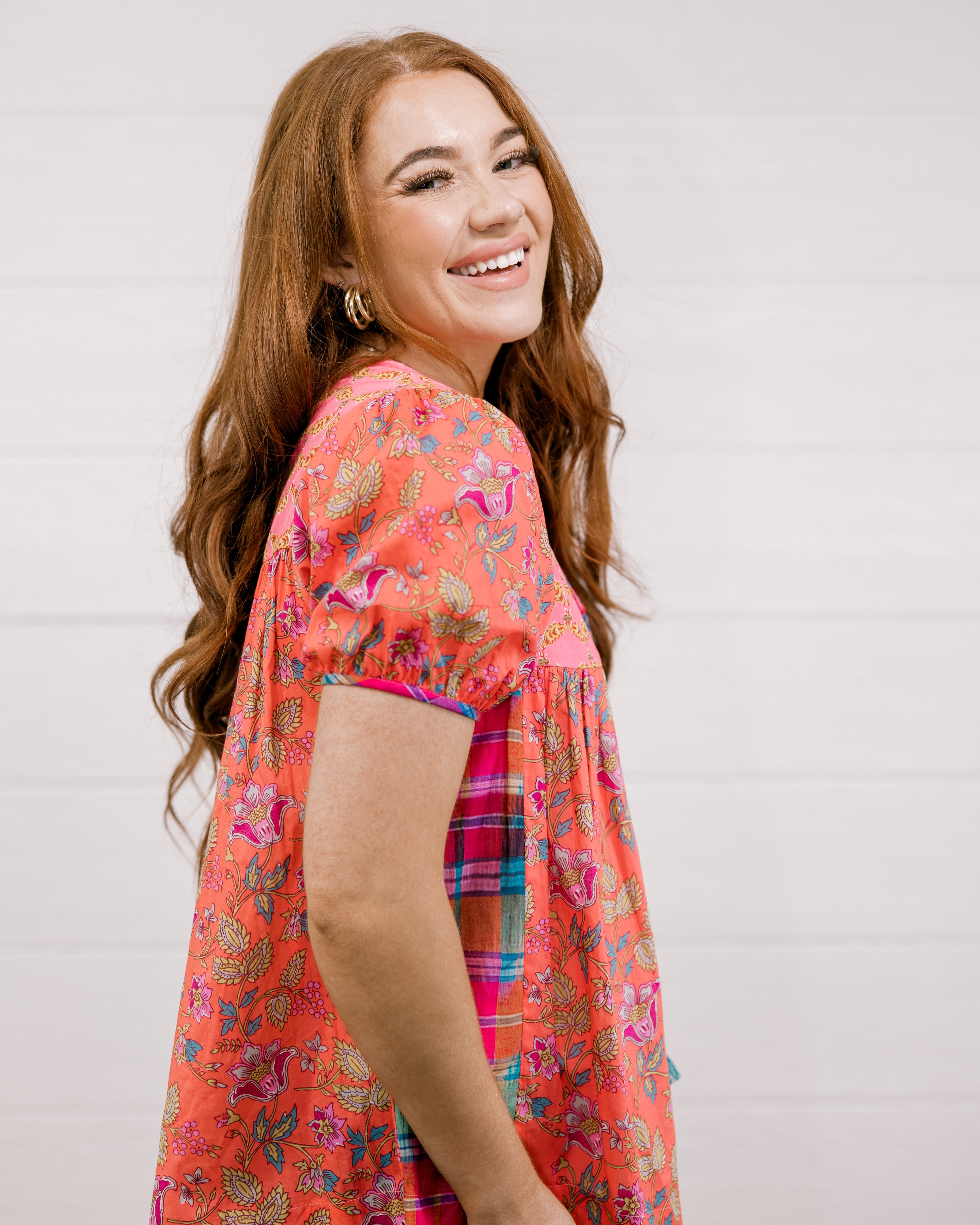 Woman wearing a colorful floral blouse against a plain background facing side. 