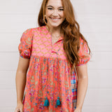 Woman wearing a colorful patterned blouse with tassels against a white background facing forward. 
