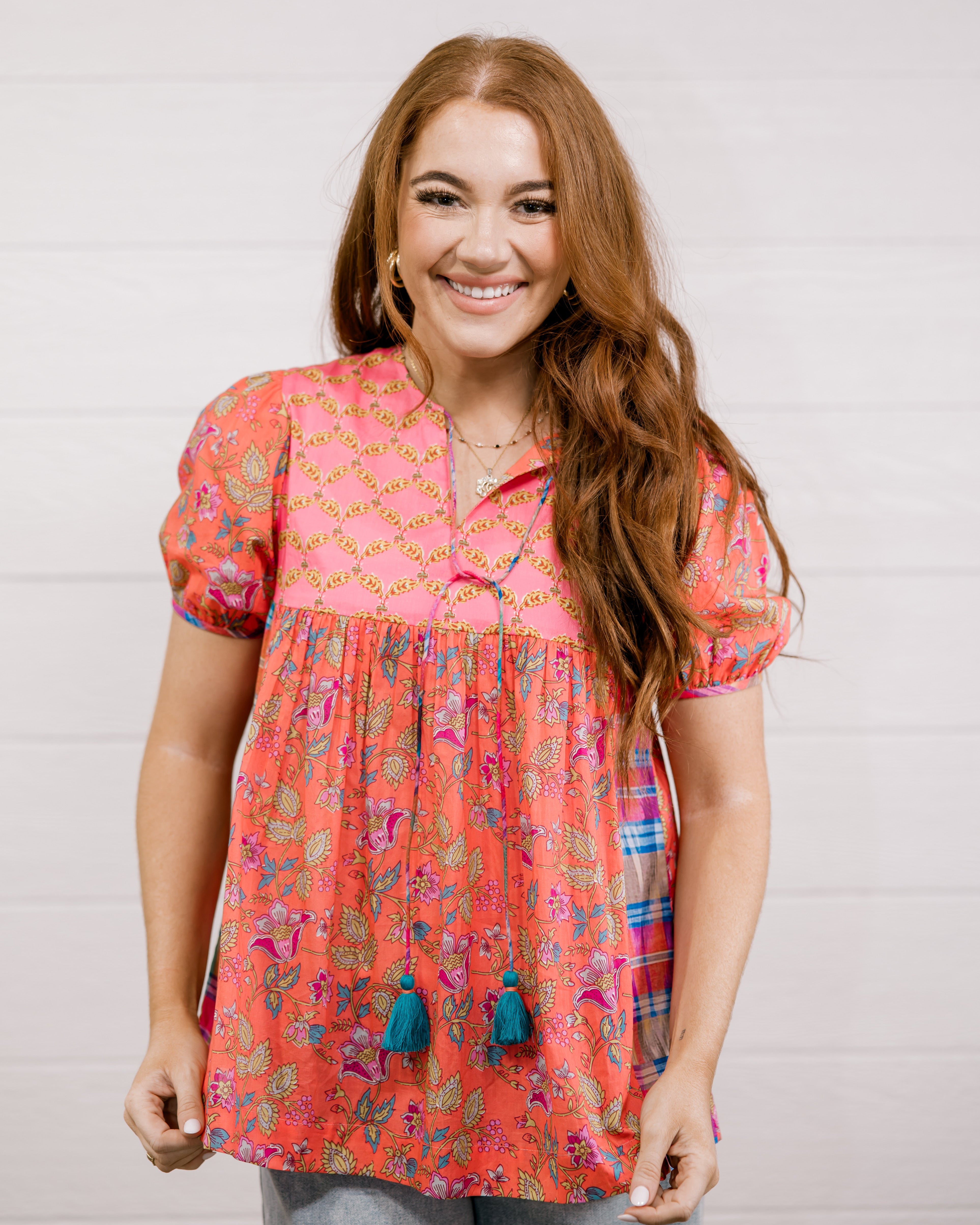 Woman wearing a colorful patterned blouse with tassels against a white background facing forward. 