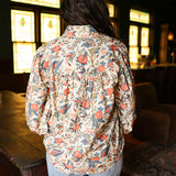 Woman with dark hair standing in a back profile position wearing the Jenna Top in a lifestyle scene. The focal point of this image is the red and blue floral pattern. The model paired this top with light-wash denim jeans. 