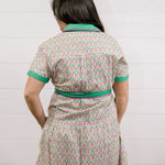 Lady wearing the a green and floral dress with pink piing and waist tie showing the back on a white background 