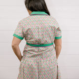 Lady wearing the a green and floral dress with pink piing and waist tie showing the back on a white background 
