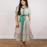 Lady wearing a green and floral mid length dress  with pink piping showing the front