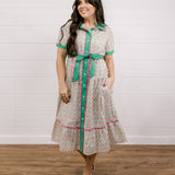 Lady wearing a green and floral mid length dress  with pink piping showing the front