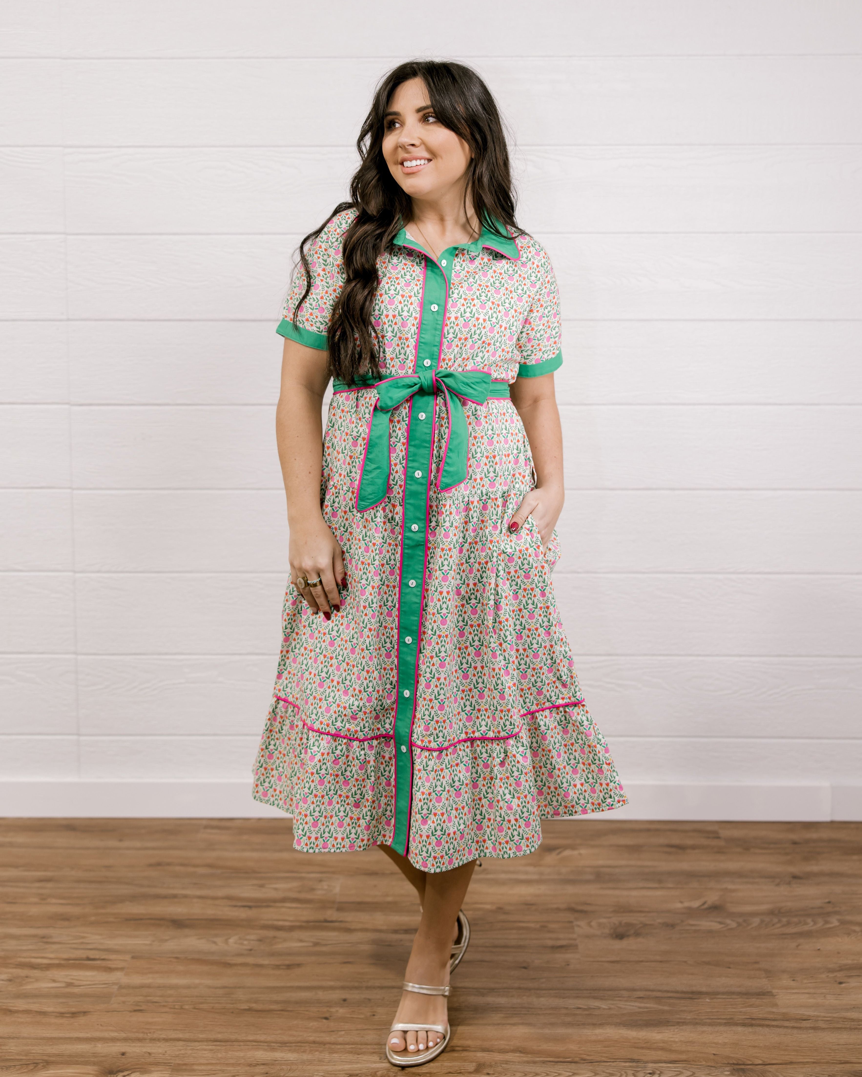 Lady wearing a green and floral mid length dress  with pink piping showing the front