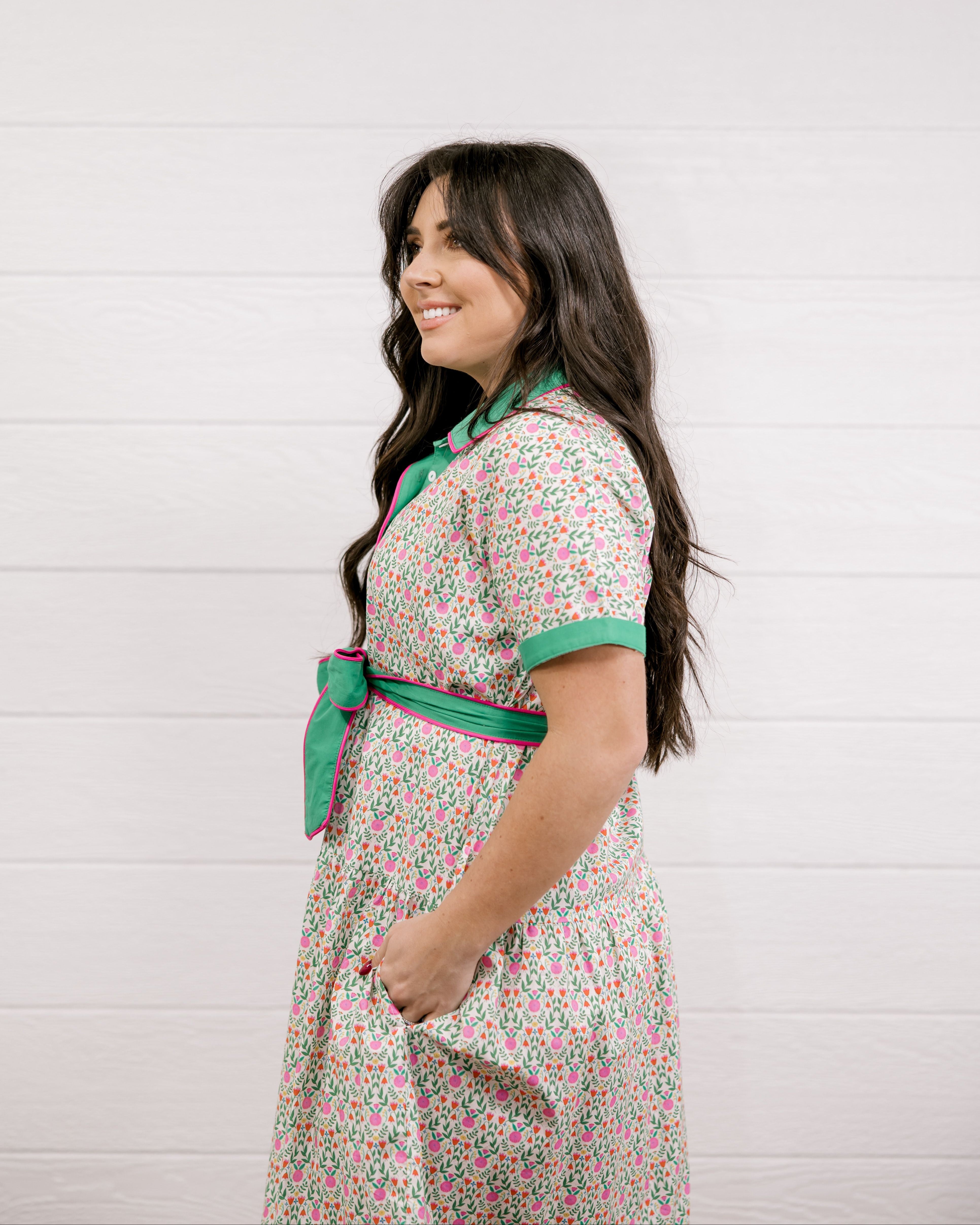 Lady wearing a green and floral dress with with pink piping showing the side and sleeve on a white background