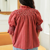 Woman with dark hair standing in a back profile position wearing the Kate Top in a lifestyle scene. The focal point of this image is the cream embroidery details on sleeve and back, ruffled collar, and striping pattern. The model paired this top with light-wash denim jeans. 