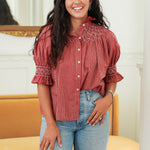Woman with dark hair standing in a front profile position wearing the Kate Top in a lifestyle scene. The focal point of this image is the embroidery on the front as well as sleeves with with ruffles. The model paired this top with light-wash denim jeans. 
