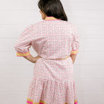Woman wearing a floral dress with a white background facing back. 