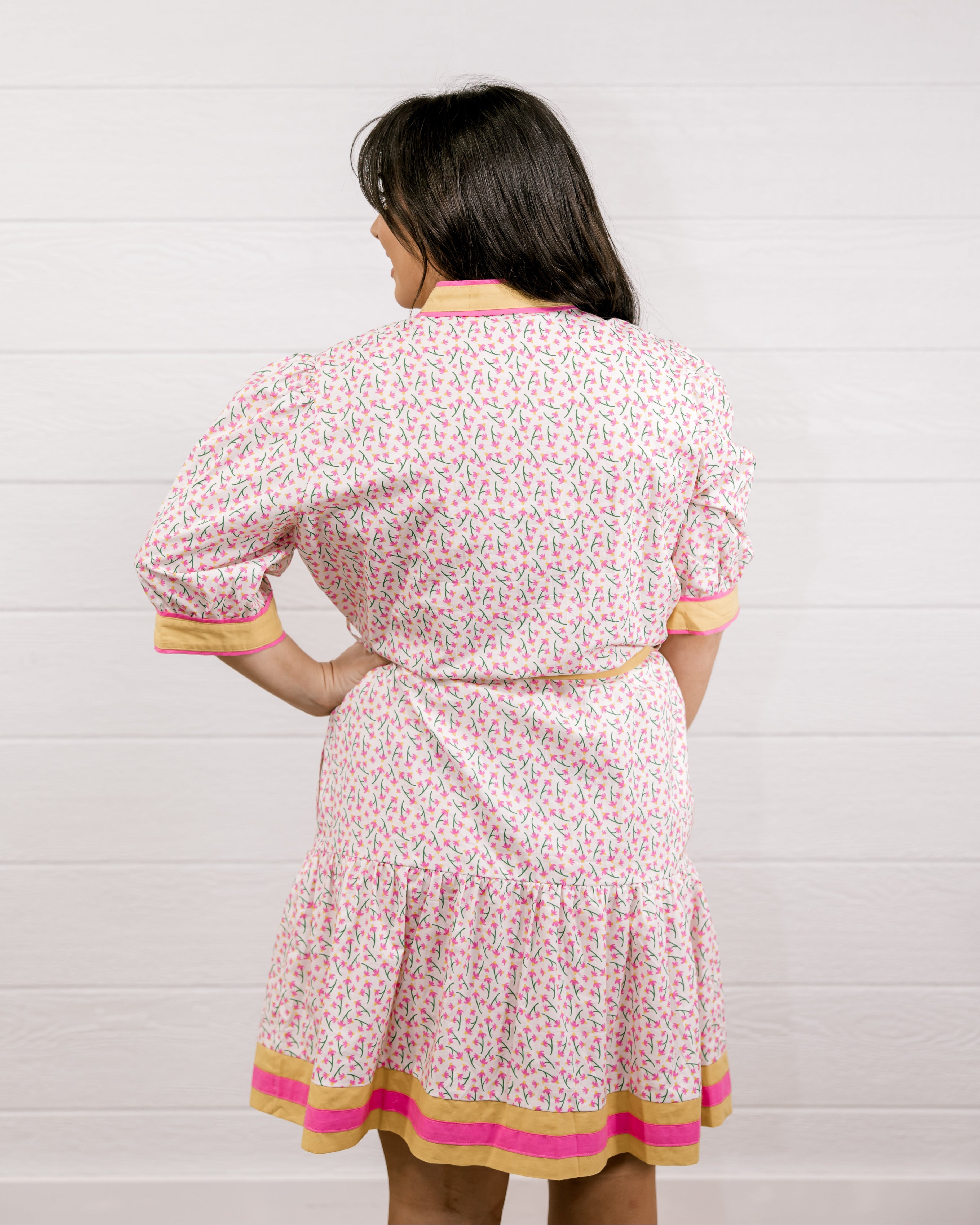 Woman wearing a floral dress with a white background facing back. 